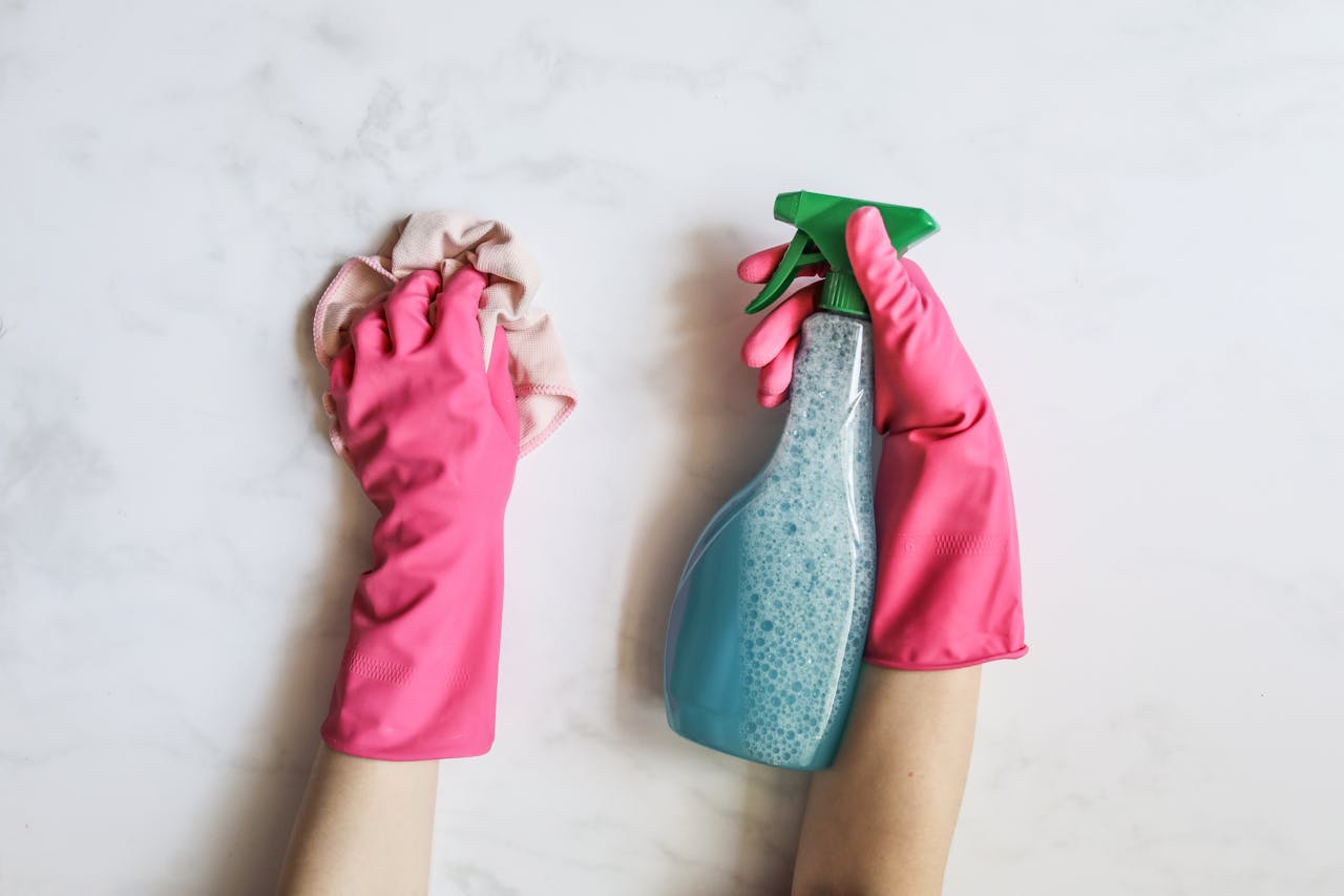 expertise-01 A pair of hands in pink gloves are cleaning with a spray bottle on a white background.